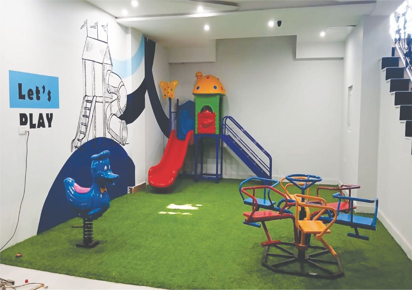 The London School indoor play area with slide, ride-ons, and 'Let's Play' wall mural