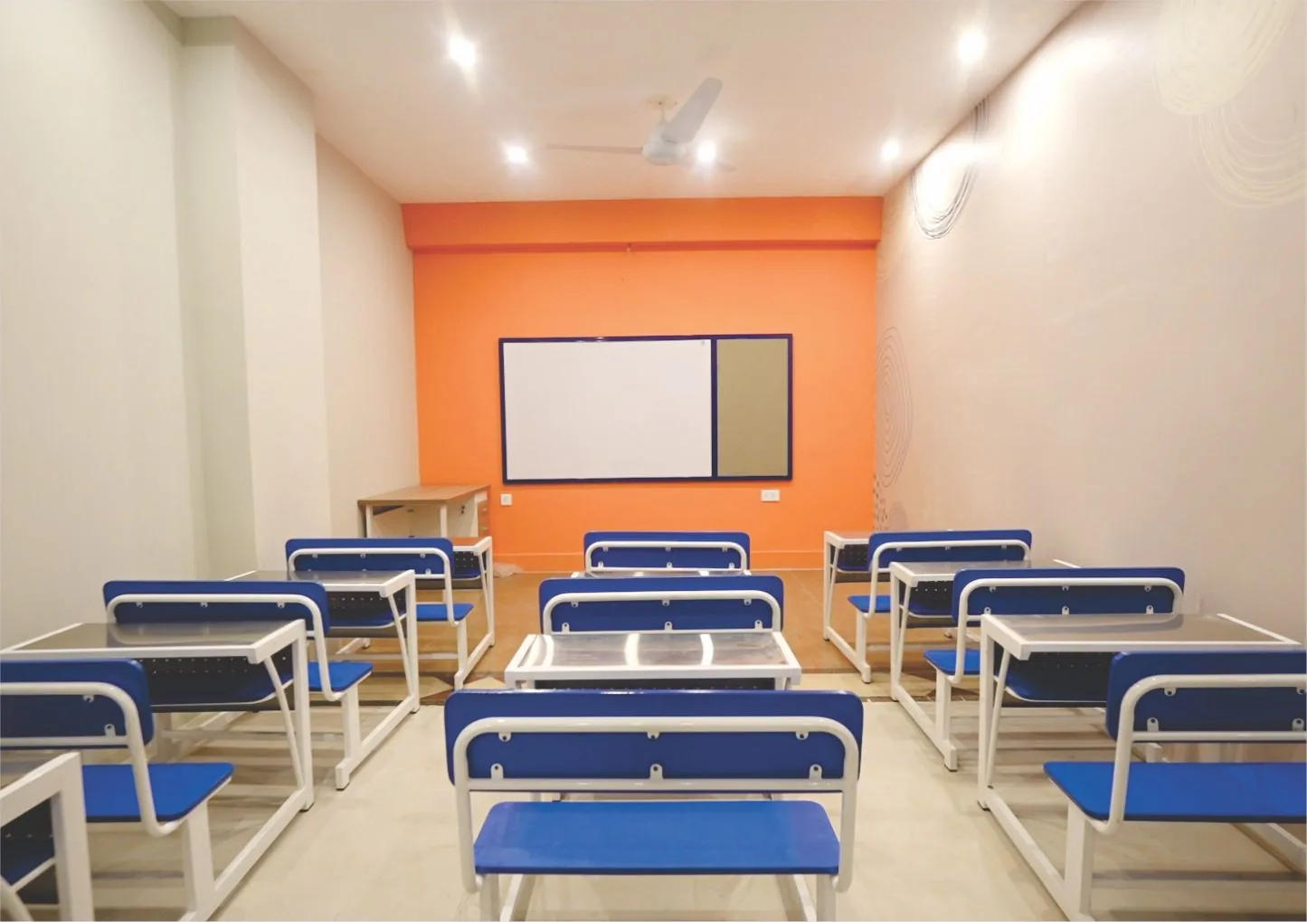 Bright Cambridge classroom at London School Lahore, with blue desks and orange accent wall